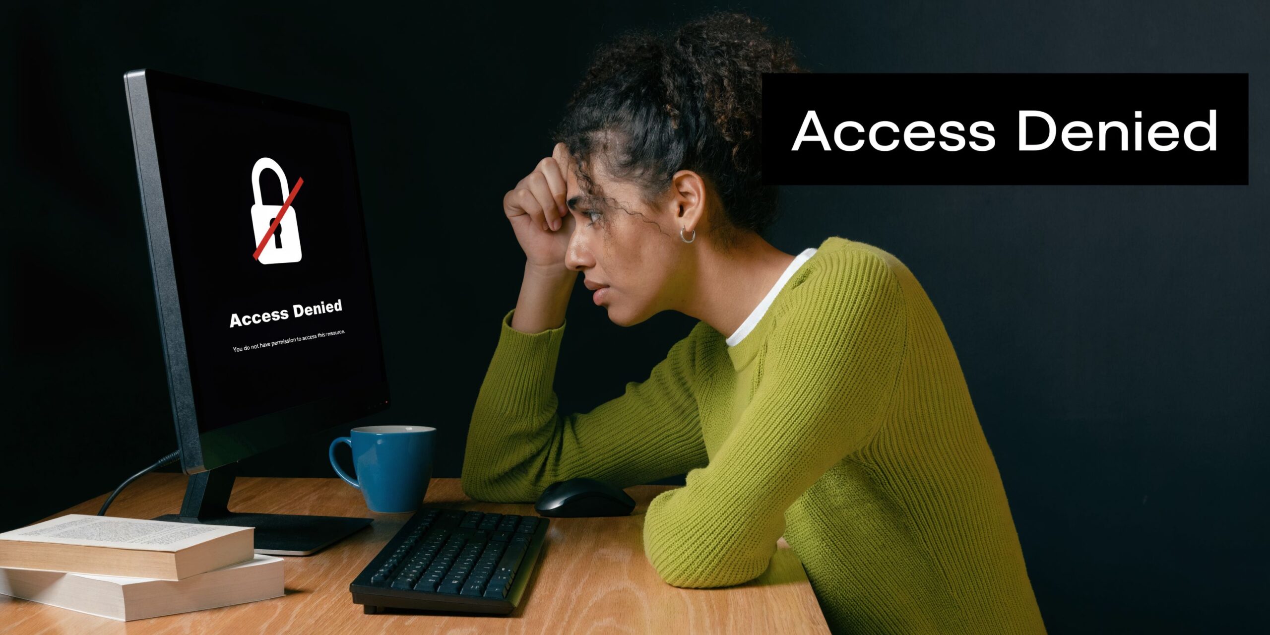 A focused woman sitting at a desk looking at a computer screen showing an access denied message.