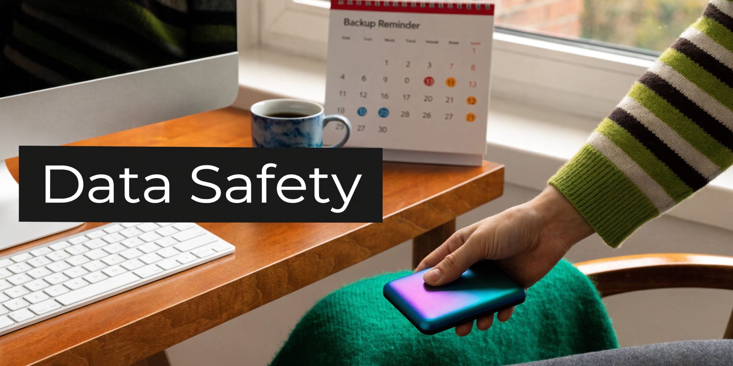 A person holding a colorful external hard drive while sitting at a desk with a backup calendar.
